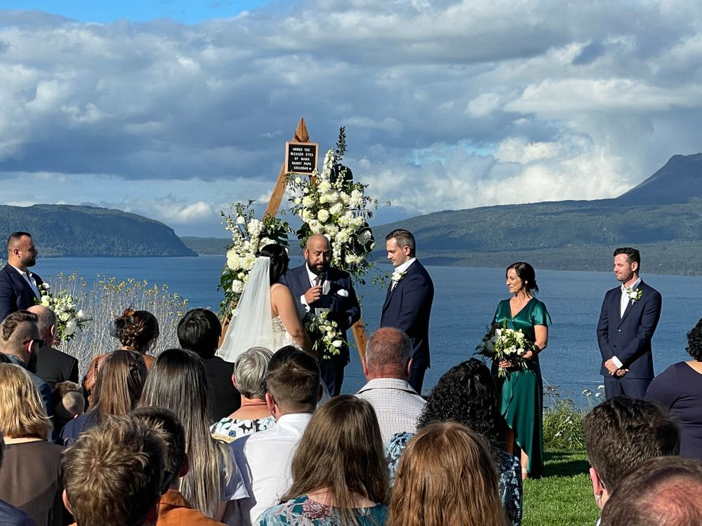 Wedding ceremony view over lake with wedding guests and wedding couple with their celebrant at The Black Barn - Tarawera Lake - Rotorua